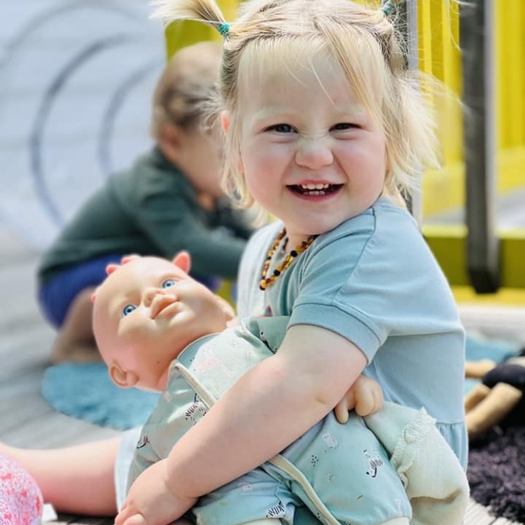 Busy Bees Alfriston Road toddler playing with a baby doll outside