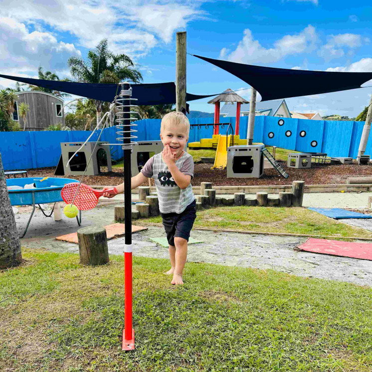 boy playing outside with tennis ball and racket at Busy Bees Coopers Beach