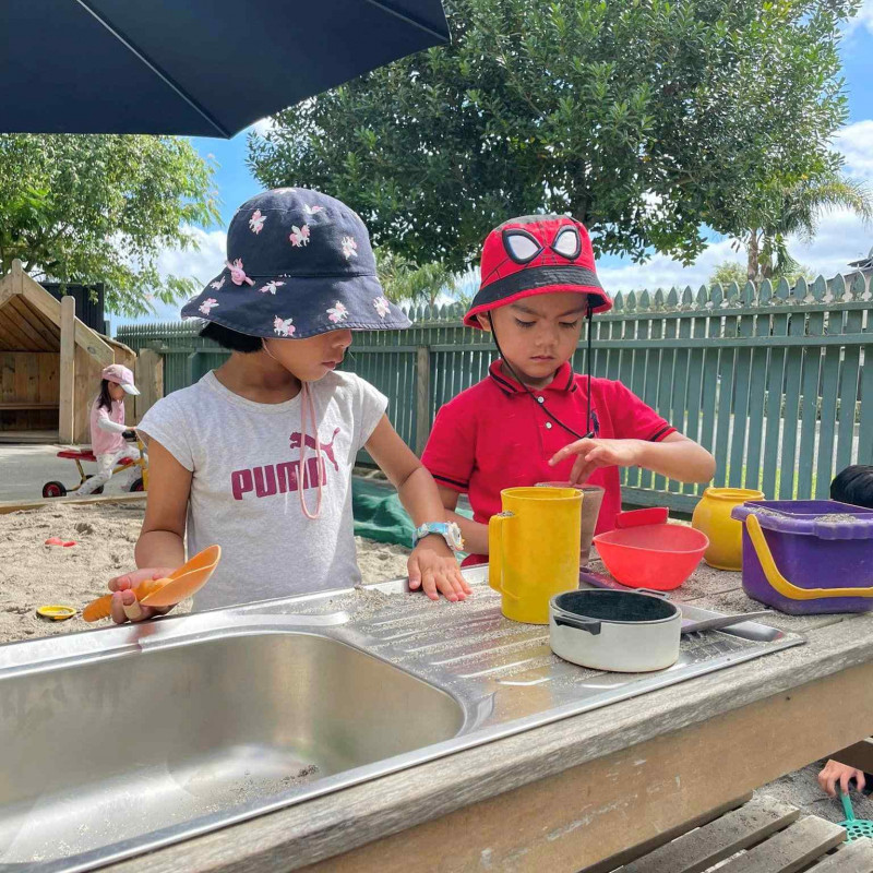 Two friends creating in the outside play kitchen at Busy Bees Napier Road